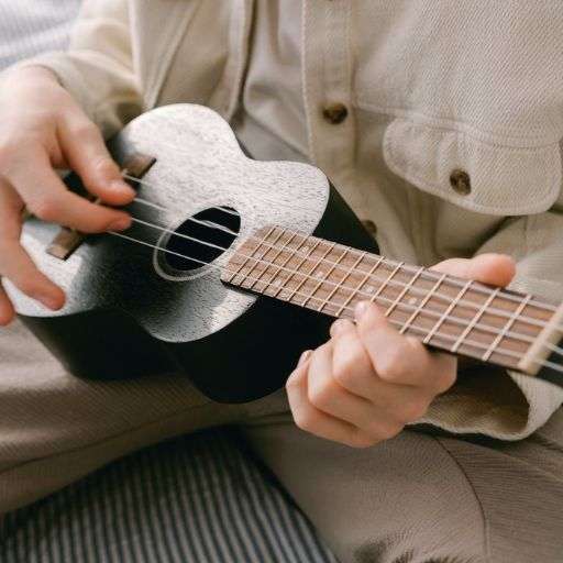 Hands playing a black ukulele close up