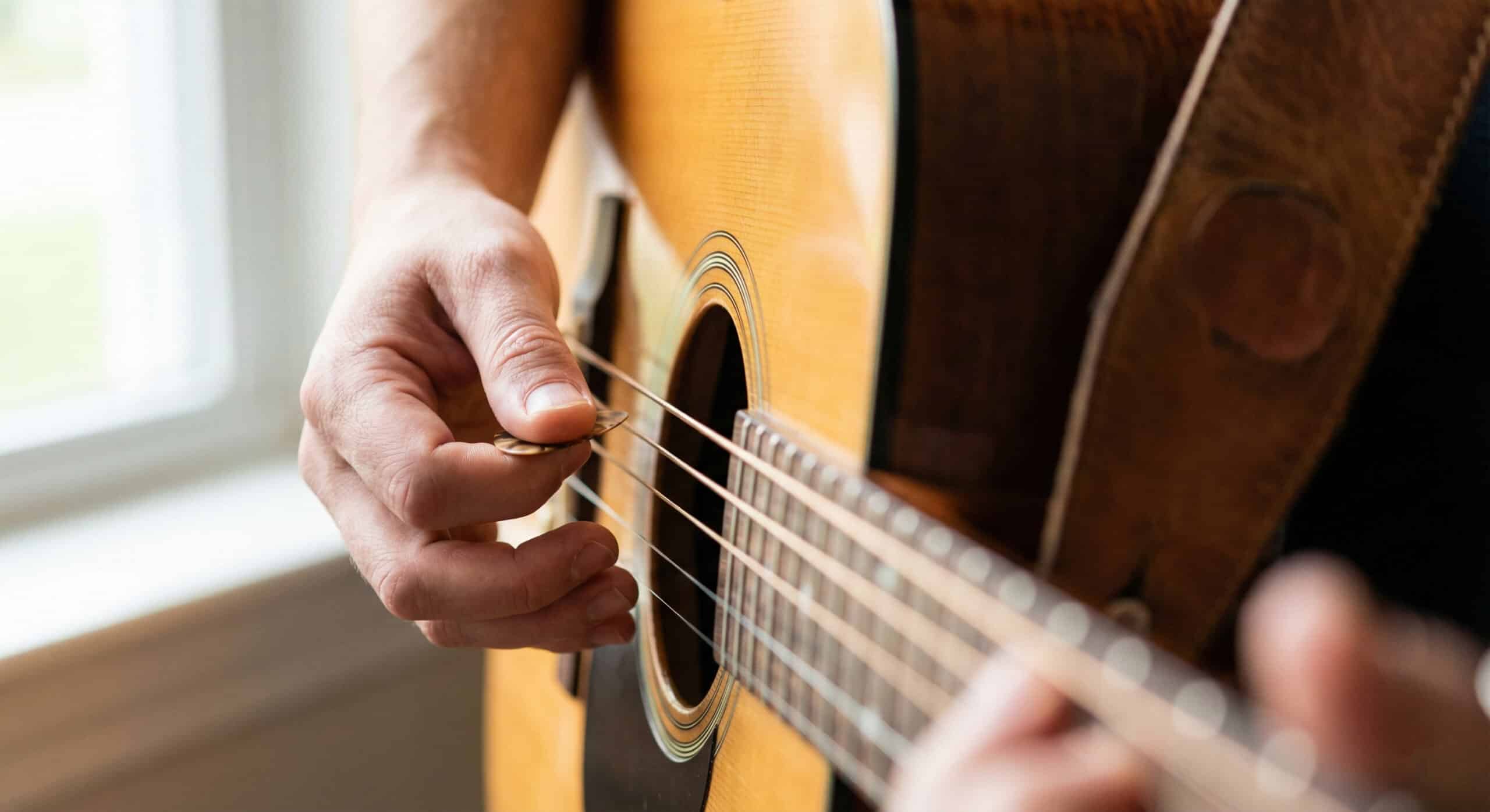 Close-up of an adult student strumming an acoustic guitar while learning proper hand technique