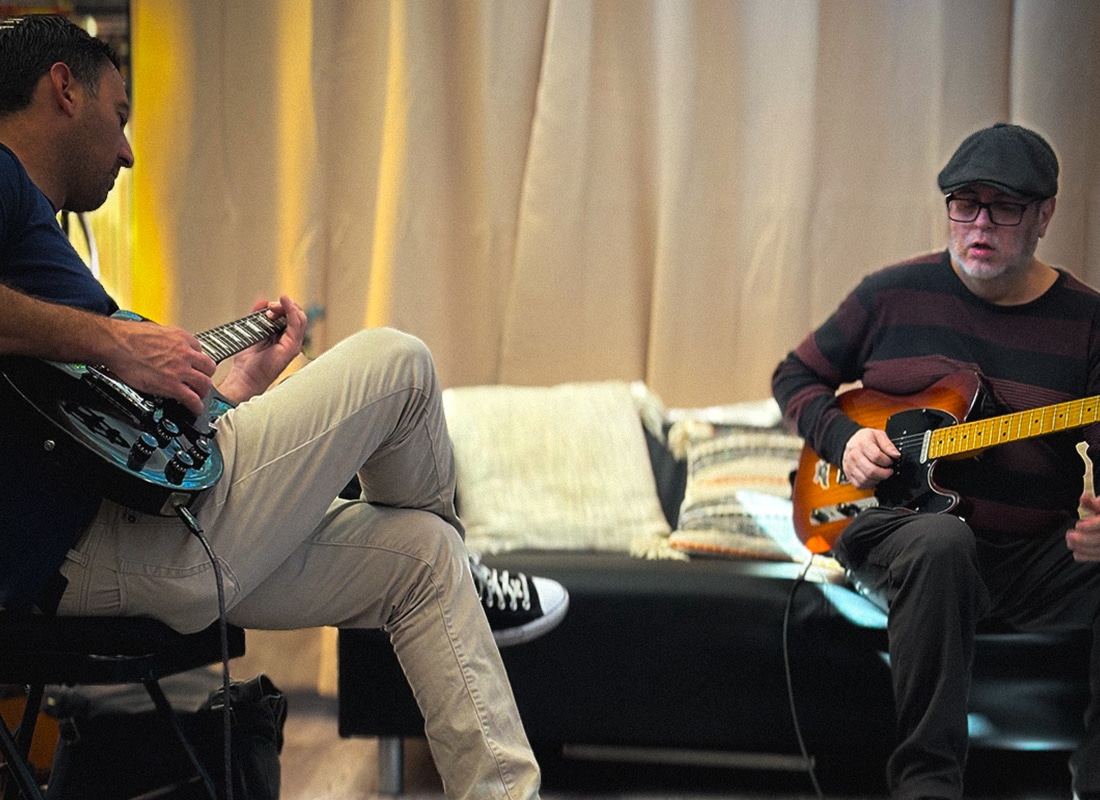 Two adult guitar students practicing electric guitar together during a focused lesson session
